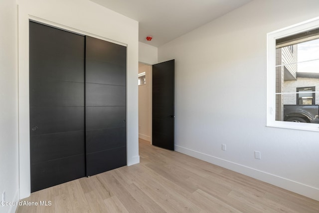 unfurnished bedroom featuring light wood-style flooring, baseboards, and a closet