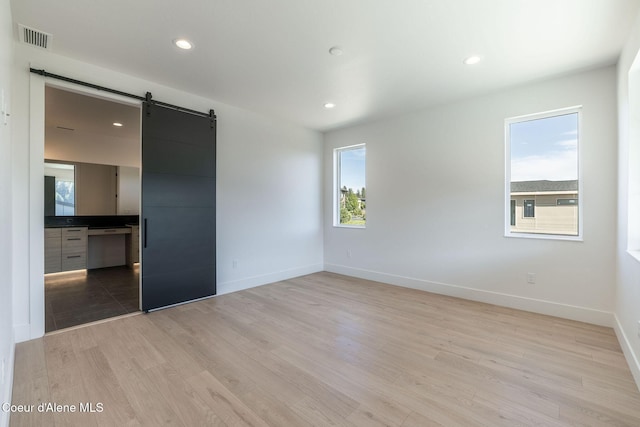 unfurnished bedroom with a barn door, multiple windows, and light wood-style flooring