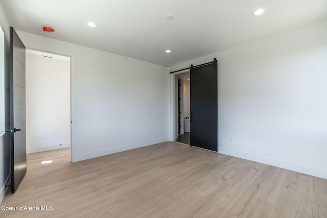 unfurnished room with baseboards, a barn door, recessed lighting, and light wood-style floors