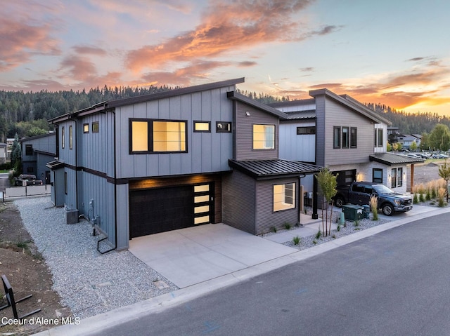 contemporary house featuring metal roof, an attached garage, concrete driveway, board and batten siding, and a standing seam roof