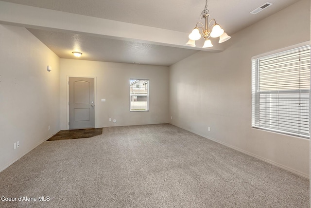 spare room featuring carpet floors, an inviting chandelier, and visible vents