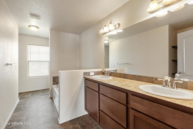 bathroom featuring a textured ceiling, double vanity, a sink, and a garden tub