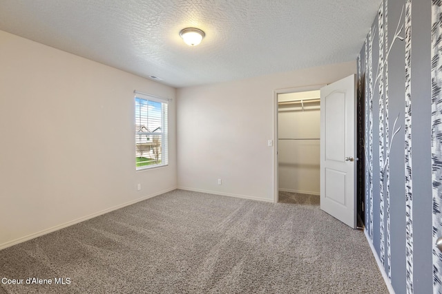 unfurnished bedroom with a textured ceiling, carpet flooring, a walk in closet, and baseboards