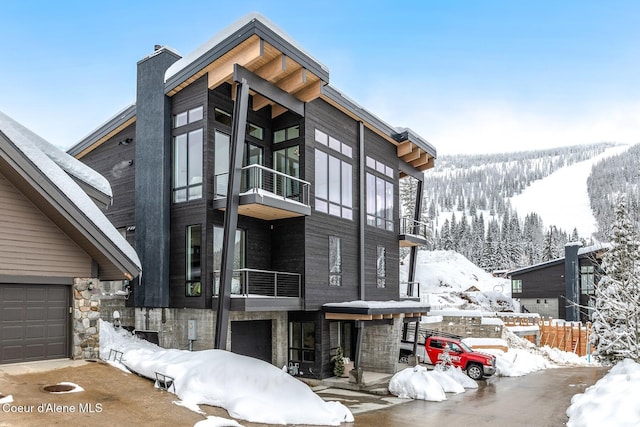 contemporary house featuring a garage, stone siding, a chimney, and a balcony