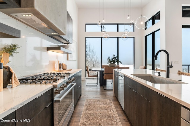 kitchen with appliances with stainless steel finishes, dark wood-type flooring, a sink, wall chimney range hood, and dark brown cabinets