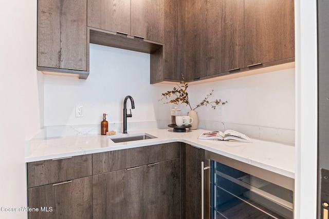 kitchen with modern cabinets, wine cooler, light stone counters, dark brown cabinets, and a sink