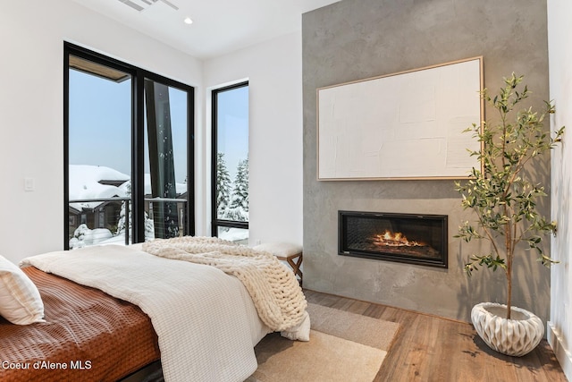 bedroom with access to exterior, a glass covered fireplace, recessed lighting, and wood finished floors