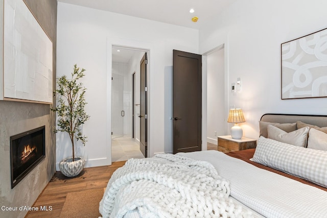 bedroom featuring a glass covered fireplace, baseboards, light wood finished floors, and recessed lighting