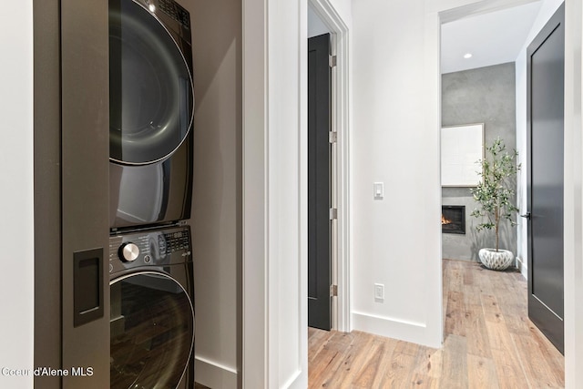 laundry room with a glass covered fireplace, laundry area, light wood-style flooring, and stacked washing maching and dryer