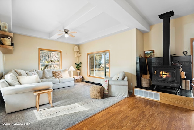 living area with ceiling fan, coffered ceiling, wood finished floors, visible vents, and a wood stove