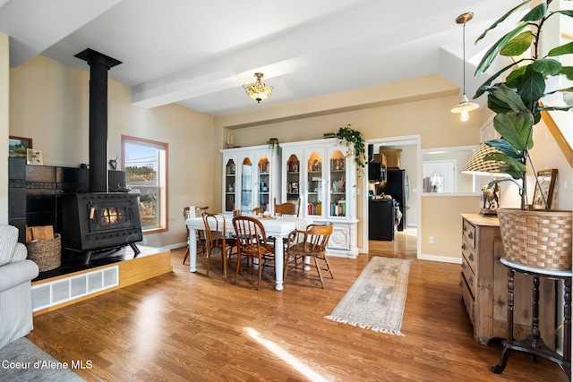 dining space with wood finished floors, visible vents, baseboards, beamed ceiling, and a wood stove