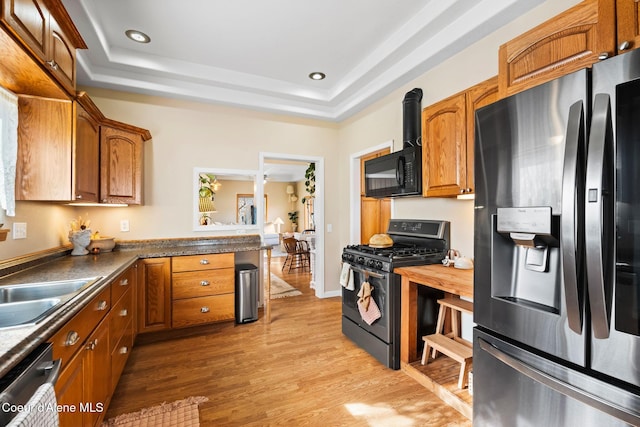 kitchen featuring light wood-type flooring, brown cabinets, appliances with stainless steel finishes, and a raised ceiling