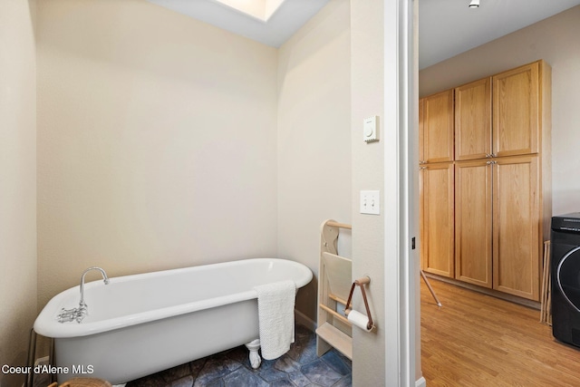 full bathroom featuring a soaking tub, wood finished floors, and washer / dryer