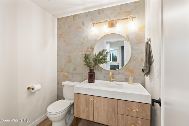 bathroom with toilet, vanity, tile walls, baseboards, and backsplash