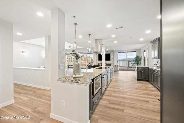 kitchen featuring light stone counters, light wood-type flooring, visible vents, and island range hood