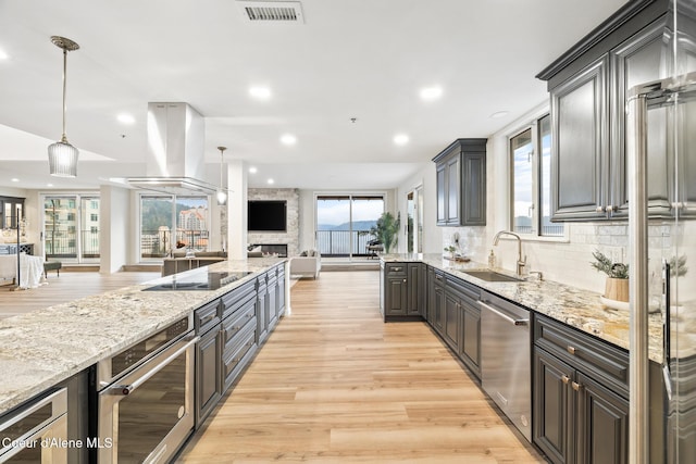 kitchen featuring island range hood, stainless steel appliances, a sink, visible vents, and open floor plan