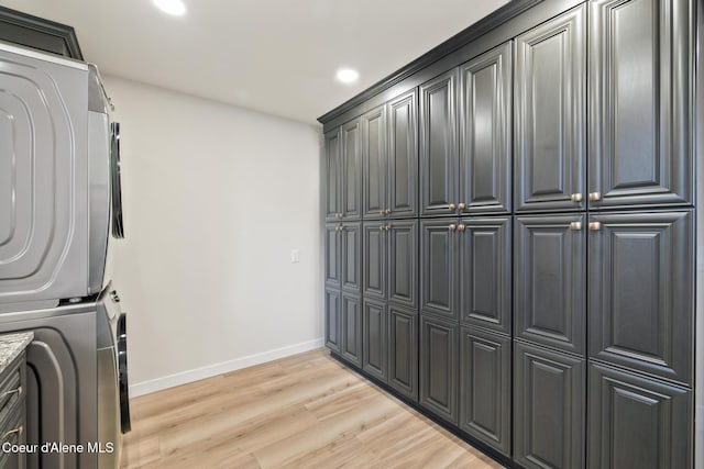 washroom featuring recessed lighting, stacked washer and dryer, baseboards, light wood-style floors, and cabinet space