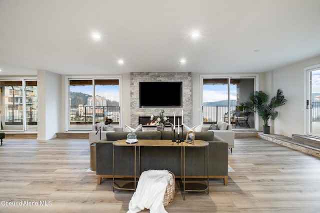 living area featuring light wood-style floors, a wealth of natural light, and a stone fireplace