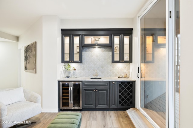 bar with light wood-style floors, beverage cooler, wet bar, and backsplash