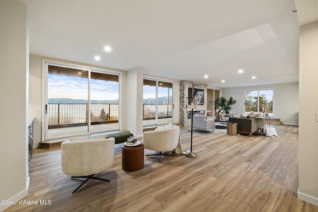 living area with light wood-type flooring, plenty of natural light, recessed lighting, and a stone fireplace