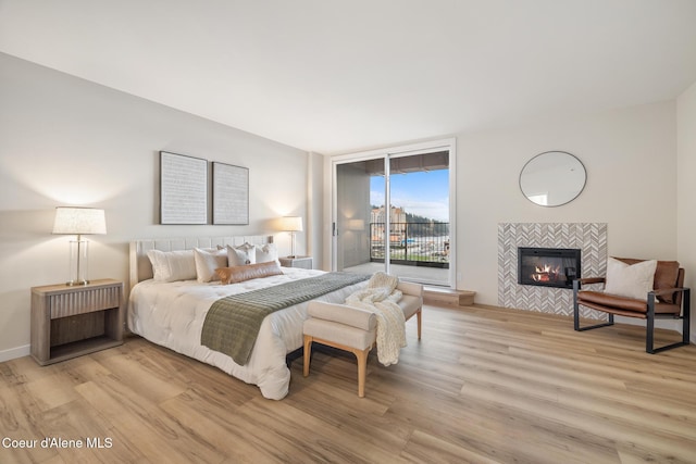 bedroom featuring access to exterior, a fireplace, light wood-style flooring, and baseboards