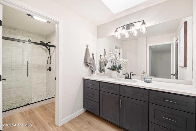 full bathroom with a skylight, a shower stall, vanity, wood finished floors, and baseboards