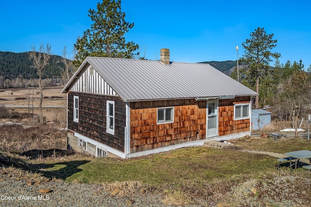 back of property with a yard, metal roof, a chimney, and a mountain view