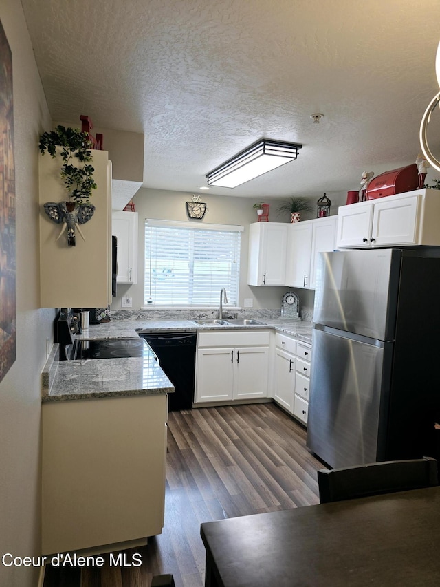 kitchen featuring dark wood-style flooring, a sink, white cabinetry, black dishwasher, and freestanding refrigerator