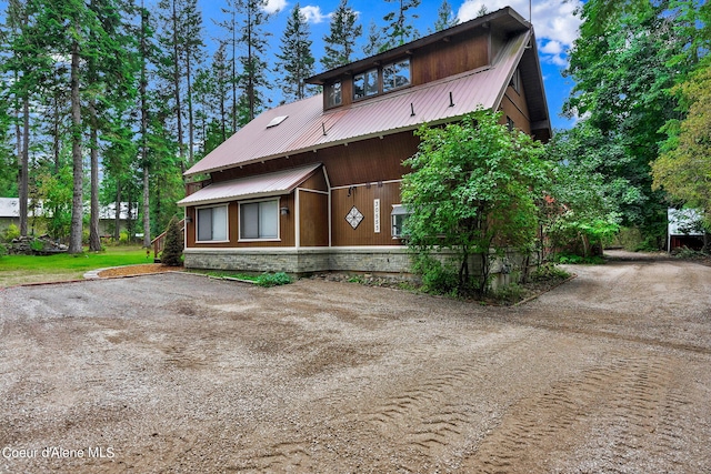 rear view of house with dirt driveway, stone siding, and metal roof