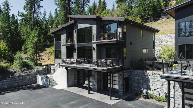 back of property featuring a patio, stairway, stone siding, and a balcony