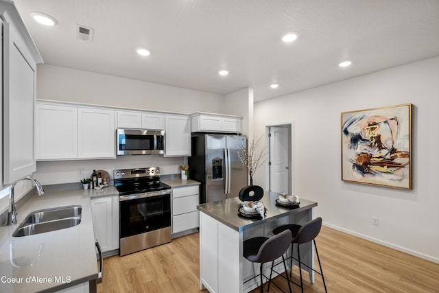 kitchen with light wood finished floors, visible vents, stainless steel appliances, white cabinetry, and a sink