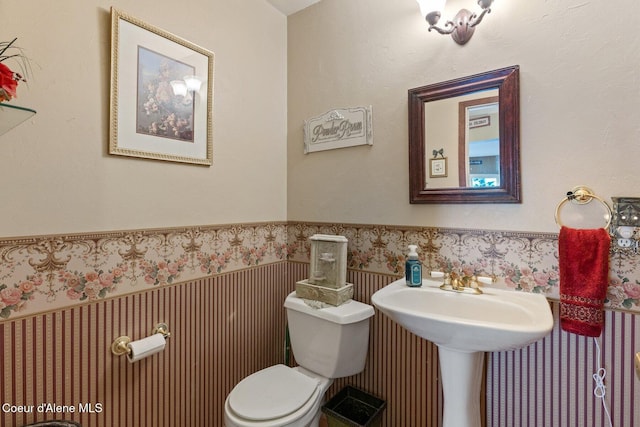 bathroom featuring a wainscoted wall, toilet, and wallpapered walls