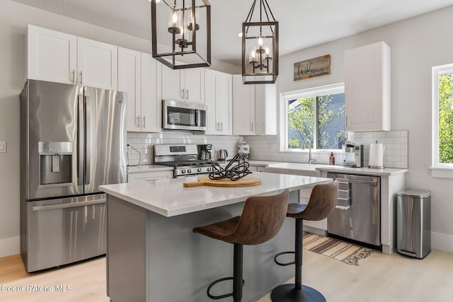 kitchen with tasteful backsplash, white cabinets, a center island, appliances with stainless steel finishes, and light wood-style floors