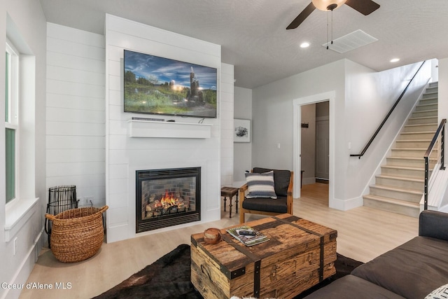 living area with visible vents, ceiling fan, stairway, and wood finished floors