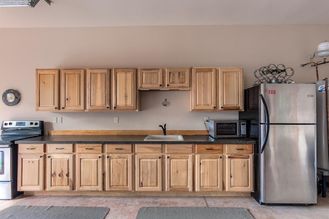 kitchen with stainless steel appliances, light brown cabinetry, dark countertops, and a sink