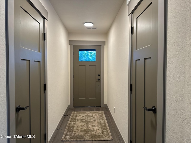 doorway featuring dark wood-type flooring, visible vents, a textured wall, and baseboards