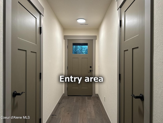 hall featuring dark wood-style floors, baseboards, visible vents, and a textured wall