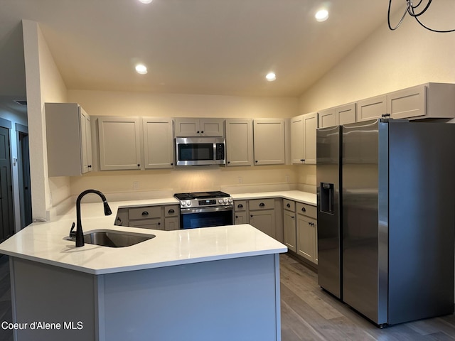 kitchen with appliances with stainless steel finishes, a peninsula, gray cabinetry, light wood-type flooring, and a sink