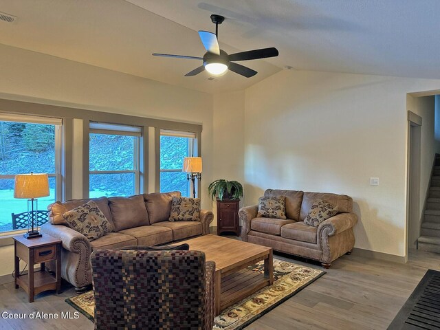 living room featuring baseboards, vaulted ceiling, light wood finished floors, and stairs