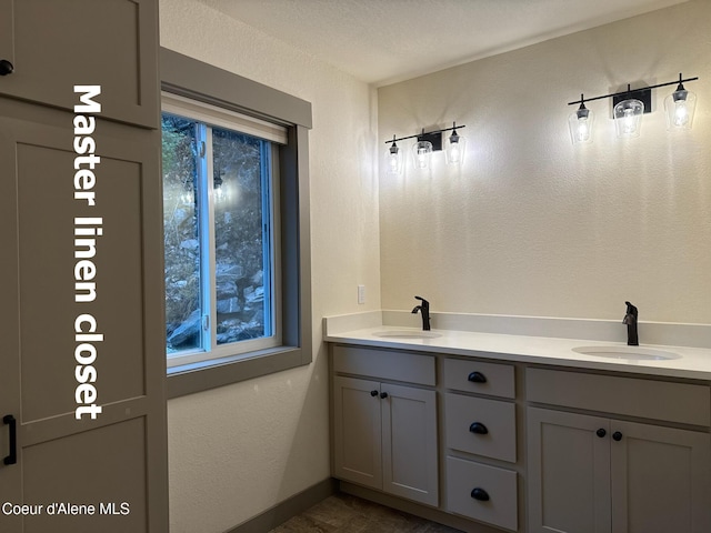 bathroom featuring a textured wall, double vanity, a sink, and baseboards