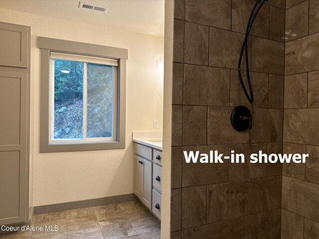 bathroom featuring vanity, a tile shower, visible vents, and baseboards