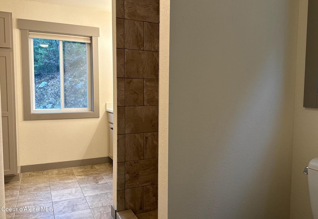 full bathroom featuring a tile shower, toilet, and baseboards