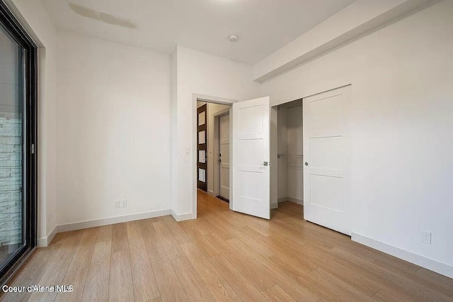 unfurnished bedroom featuring light wood finished floors, a closet, and baseboards