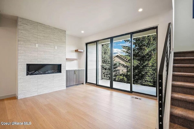 unfurnished living room with recessed lighting, visible vents, a large fireplace, light wood-type flooring, and stairs