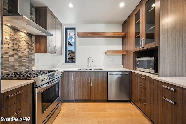 kitchen featuring open shelves, a sink, light wood-style floors, appliances with stainless steel finishes, and wall chimney exhaust hood