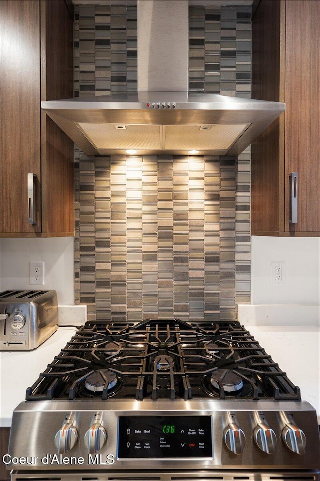 kitchen with wall chimney exhaust hood, stainless steel gas range oven, light countertops, and decorative backsplash