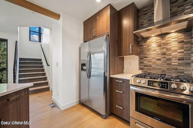 kitchen with light countertops, decorative backsplash, appliances with stainless steel finishes, light wood-style floors, and wall chimney range hood