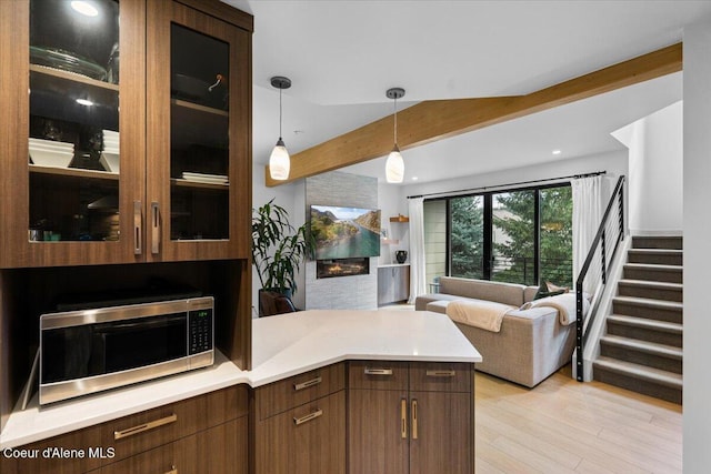 kitchen featuring a peninsula, open floor plan, beamed ceiling, light countertops, and stainless steel microwave