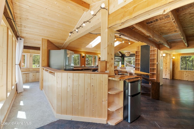 kitchen with vaulted ceiling with skylight, wood walls, wooden ceiling, and freestanding refrigerator