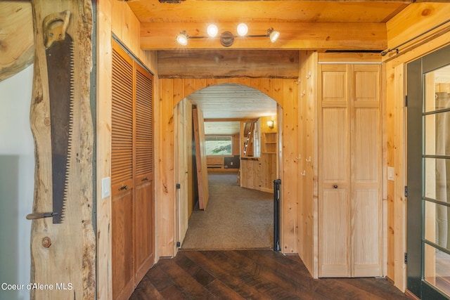 hallway featuring arched walkways, beamed ceiling, dark wood-style floors, and wooden walls